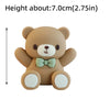 A small, light brown teddy bear cake topper with a green bow and white paws.