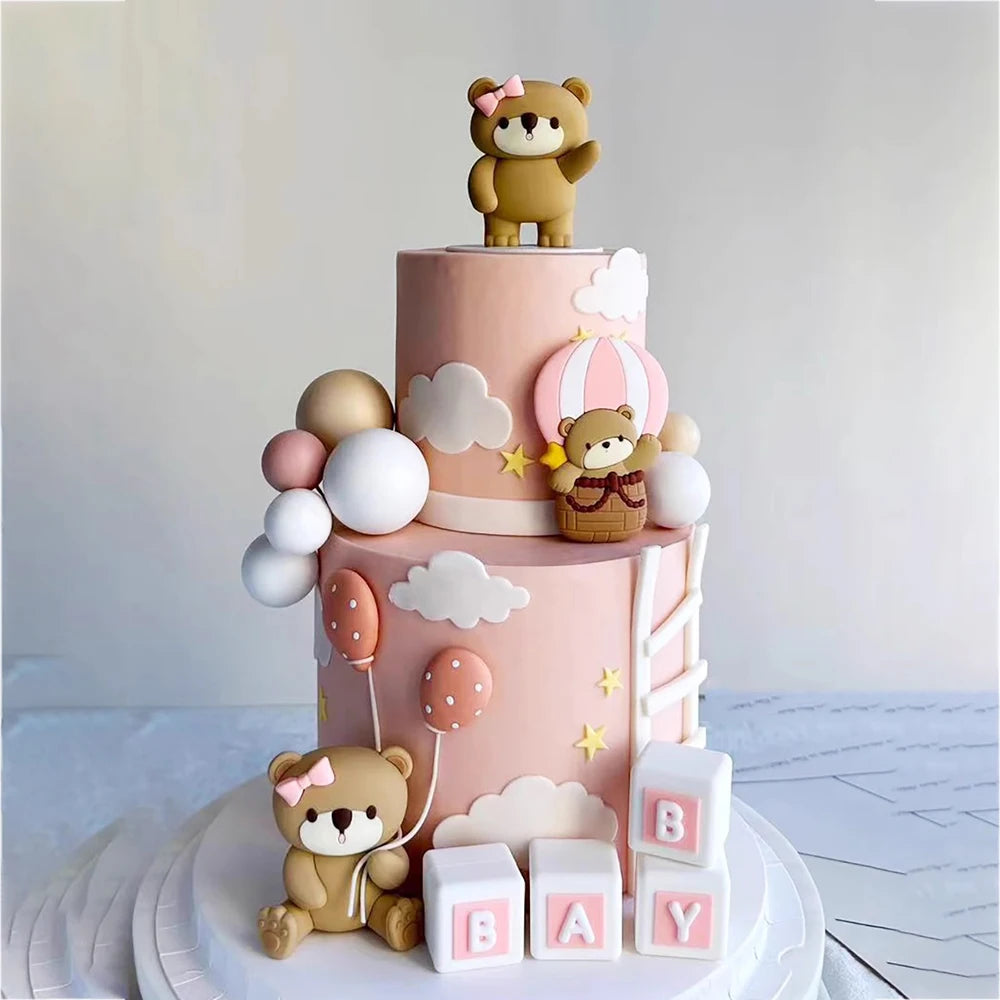 A tiered pink cake decorated with bear figures and clouds for a birthday or baby shower