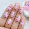 A hand displays several small pink resin teddy bear charms for DIY crafts.