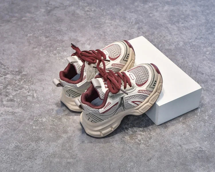 A pair of red and beige breathable mesh kids running sneakers resting on a white box.