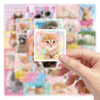 A hand holds a square card featuring a cute orange kitten surrounded by pastel floral borders and stars.