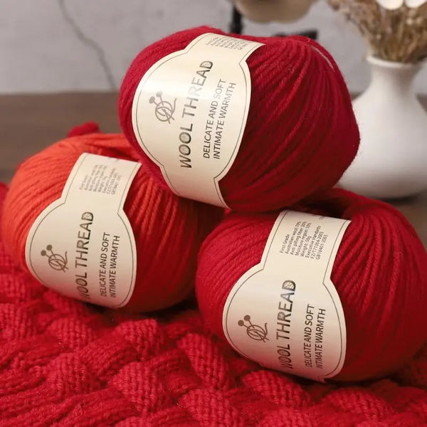 A ball of red wool thread labeled Wool Thread delicate and soft intimate warmth resting on a red knitted fabric.