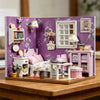 A DIY wooden miniature dollhouse kit featuring pink furniture and purple floral wallpaper.