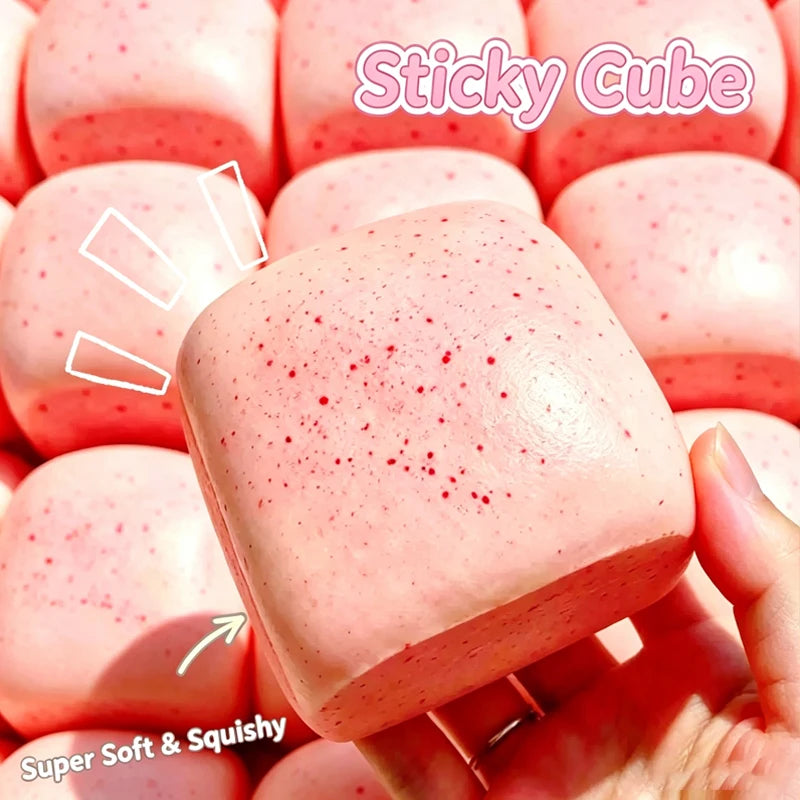 A close-up of a pink sticky cube squishy toy being held in a hand, showing its soft texture and speckled surface.