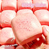 A close-up of a pink sticky cube squishy toy being held in a hand, showing its soft texture and speckled surface.
