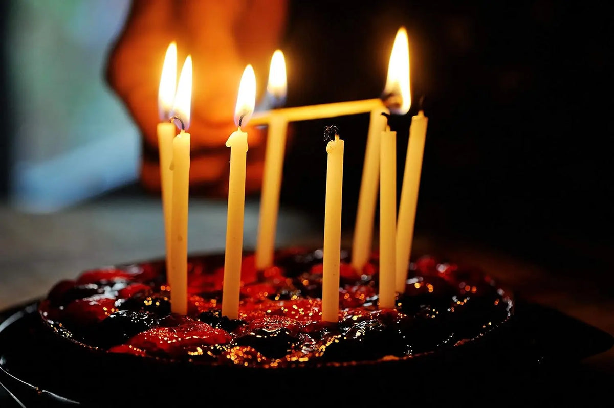A plate of red cake decorated with lit natural beeswax taper candles in a dark setting.