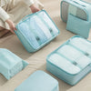 A set of light blue travel packing cubes and storage bags are displayed on a beige surface.