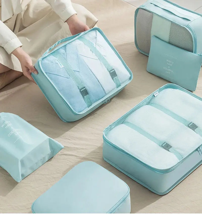 A set of light blue travel packing cubes and storage bags are displayed on a beige surface.