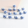 A set of twenty round ceramic flower beads in blue and white patterns arranged on a light pink surface.