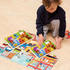 A young child is assembling a wooden tangram puzzle set featuring animals, vehicles, and sea life on the floor.