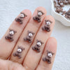 A hand displays several small, fuzzy grey resin teddy bear charms for DIY crafts.