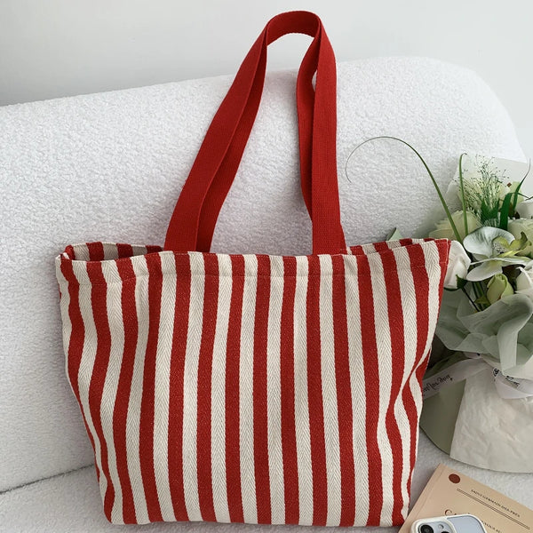 A red and off-white striped canvas shoulder tote bag resting on a white surface.