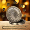A round, antique-style metal case featuring a dragon design, surrounded by seven small dice, next to a silver chain.