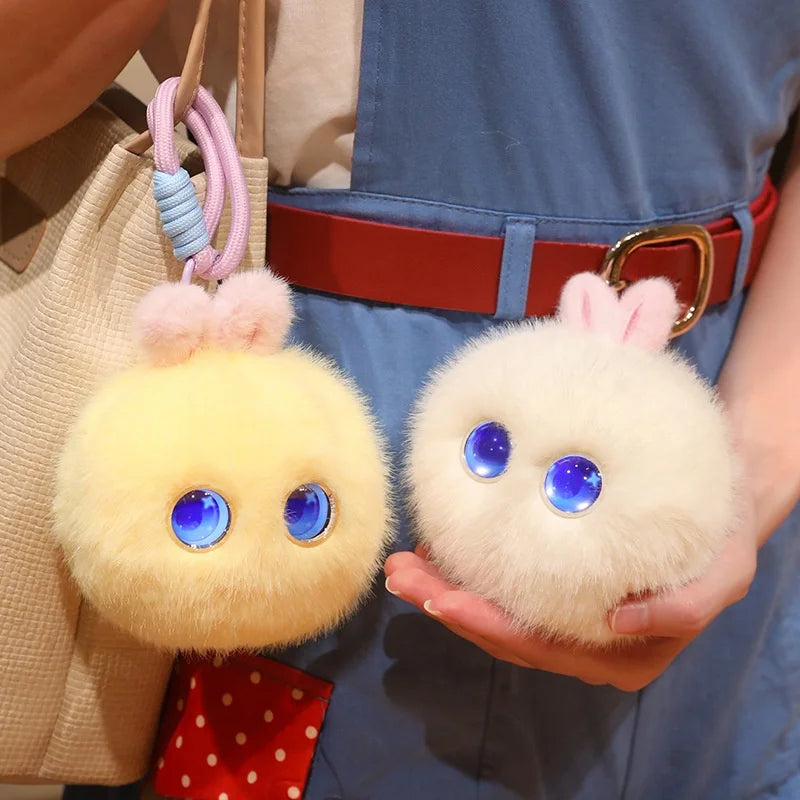 A fluffy white rabbit plush pendant with blue eyes is held in a person's hand against a blue apron.