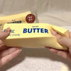 A hand holds a yellow butter squishy toy labeled salted butter with a limited edition stamp.