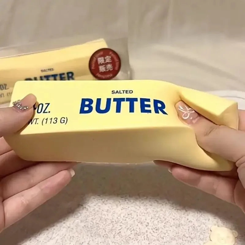 A hand holds a yellow butter squishy toy labeled salted butter with a limited edition stamp.