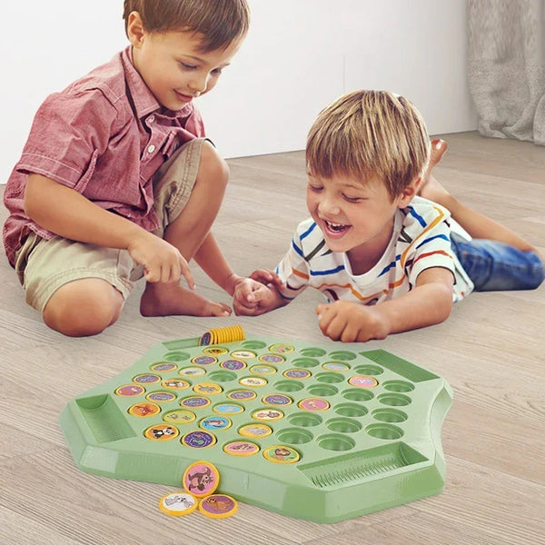 Two young boys playing with a green interactive chess set on a wooden floor.