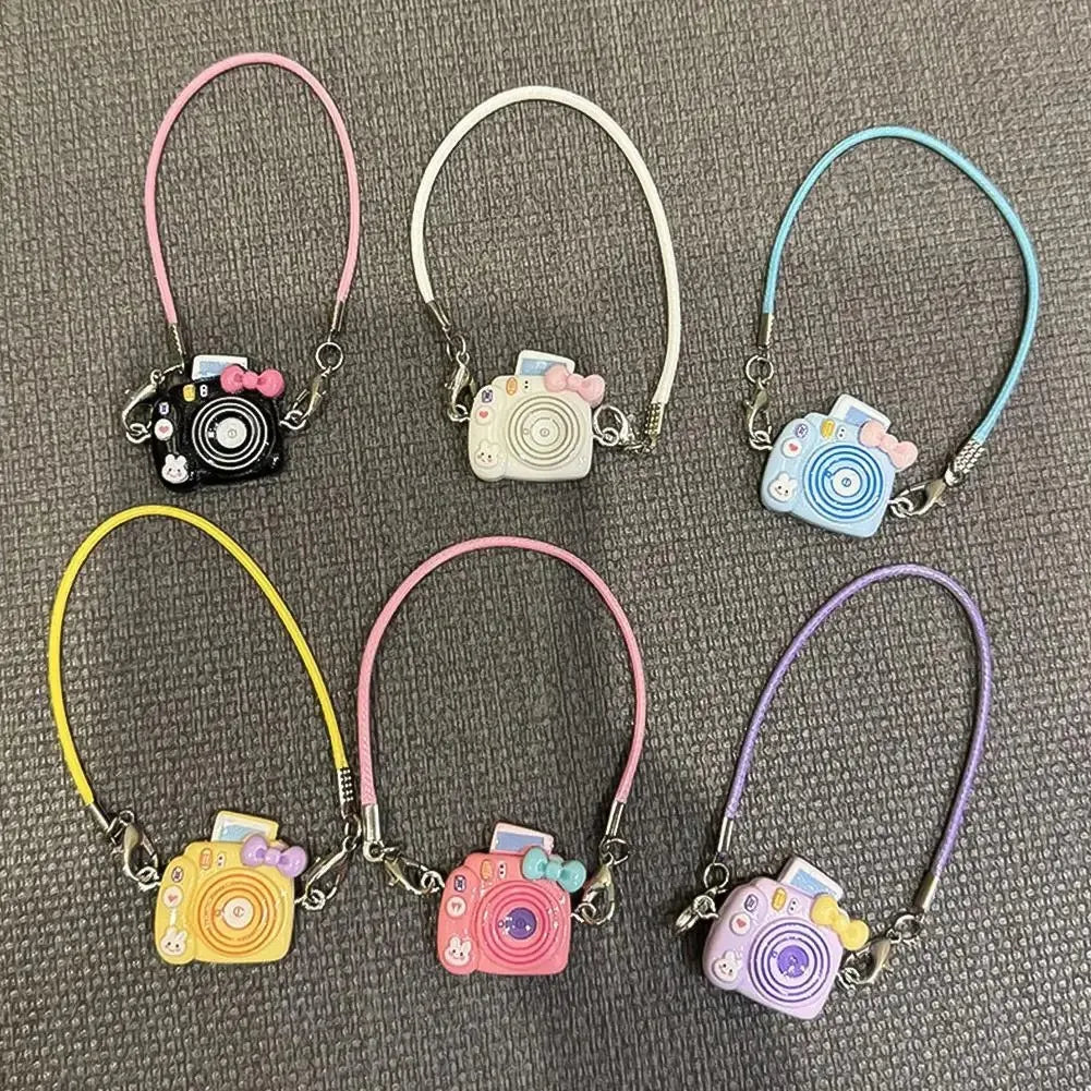 A collection of nine thin silver necklaces featuring small camera-themed charms and pink, white, and blue colored cord.