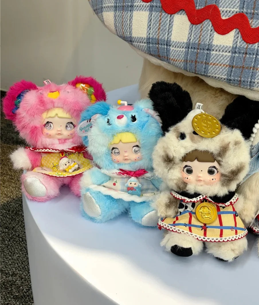 Three fluffy collectible dolls with pink, blue, and white fur are displayed next to a plaid hat.