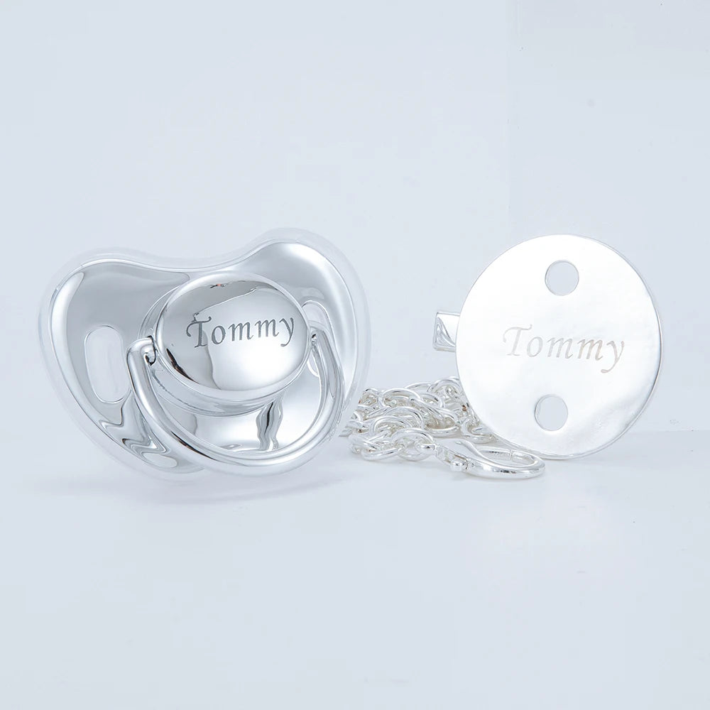 Silver pacifier clip set with a heart-shaped pacifier and a round clip, both engraved with the name Tommy