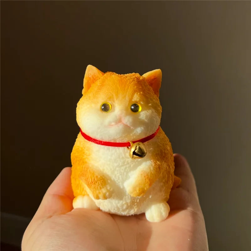 A small, orange cat-shaped squishy stress relief toy with yellow eyes and a red collar is held in a hand.