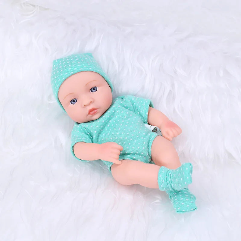 A realistic soft vinyl reborn baby doll wearing a mint green outfit and hat, lying on white fluffy material.
