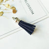 A silver tassel with dark navy velvet fibers rests on a white card with the word BLOSSOM.