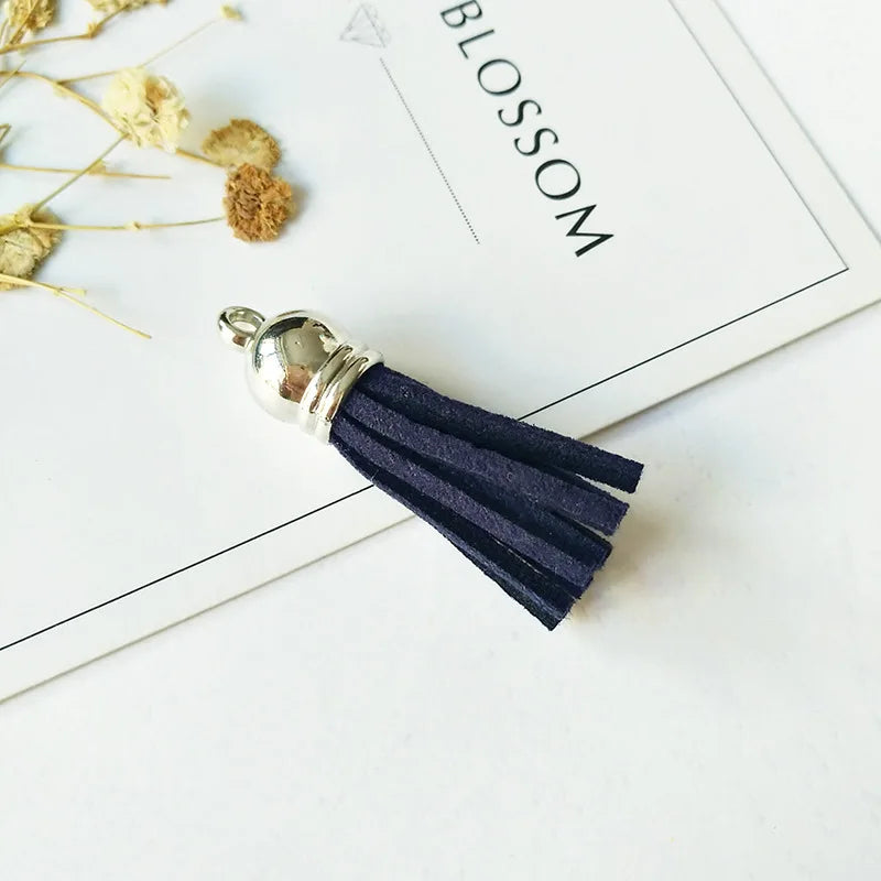 A silver tassel with dark navy velvet fibers rests on a white card with the word BLOSSOM.