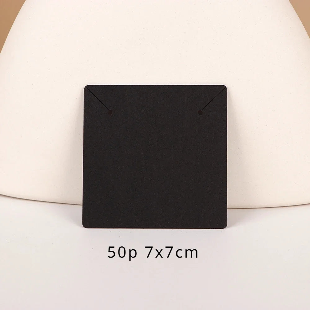 A black square jewelry display card is shown on a light beige surface.