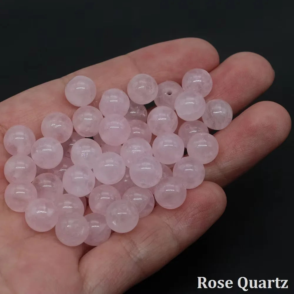 A hand holds a cluster of round, translucent pink rose quartz beads for jewelry making.