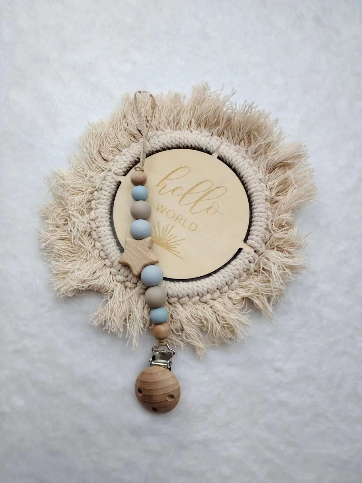 A personalized wooden baby pacifier clip featuring silicone beads and a natural fiber wreath with the words hello world
