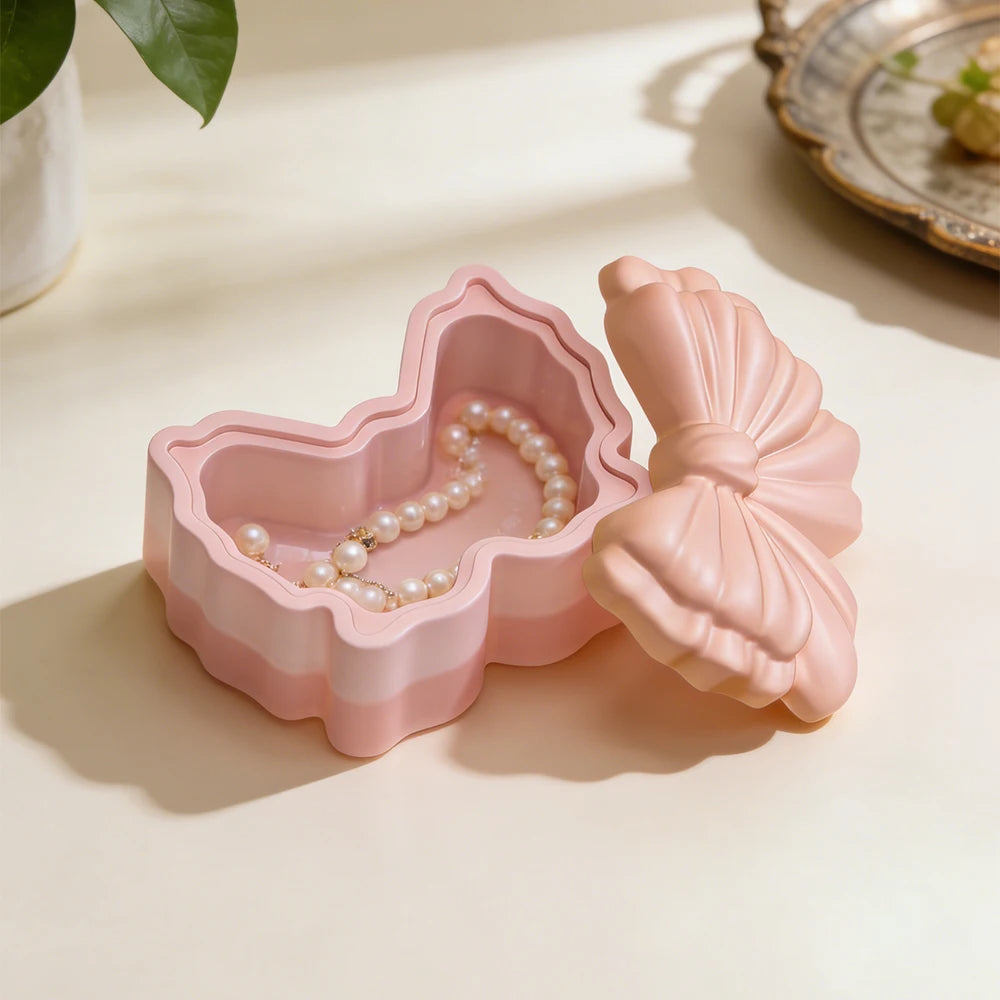 A pink silicone resin mold shaped like a bowknot with a lid, featuring a striped pattern and a pearl necklace inside.