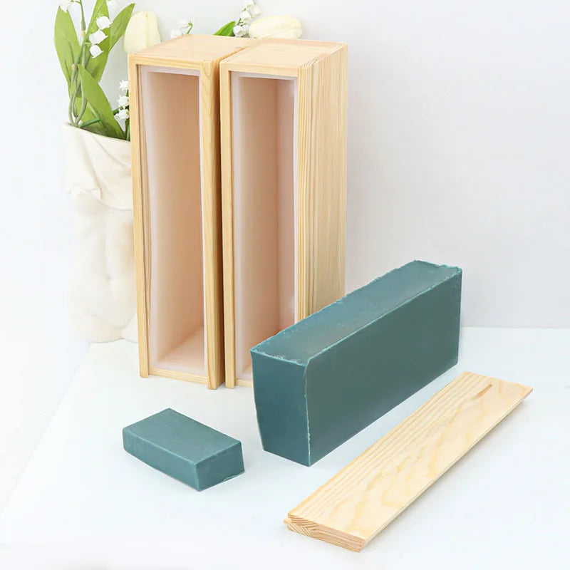 A silicone rectangle soap mold is shown with a wooden box and lid, alongside a wooden plank.