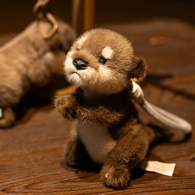 A small, brown plush otter charm resting on a wooden surface.