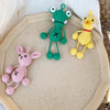 Three handmade crochet frog ornaments in green, yellow, and pink resting on a light beige surface.