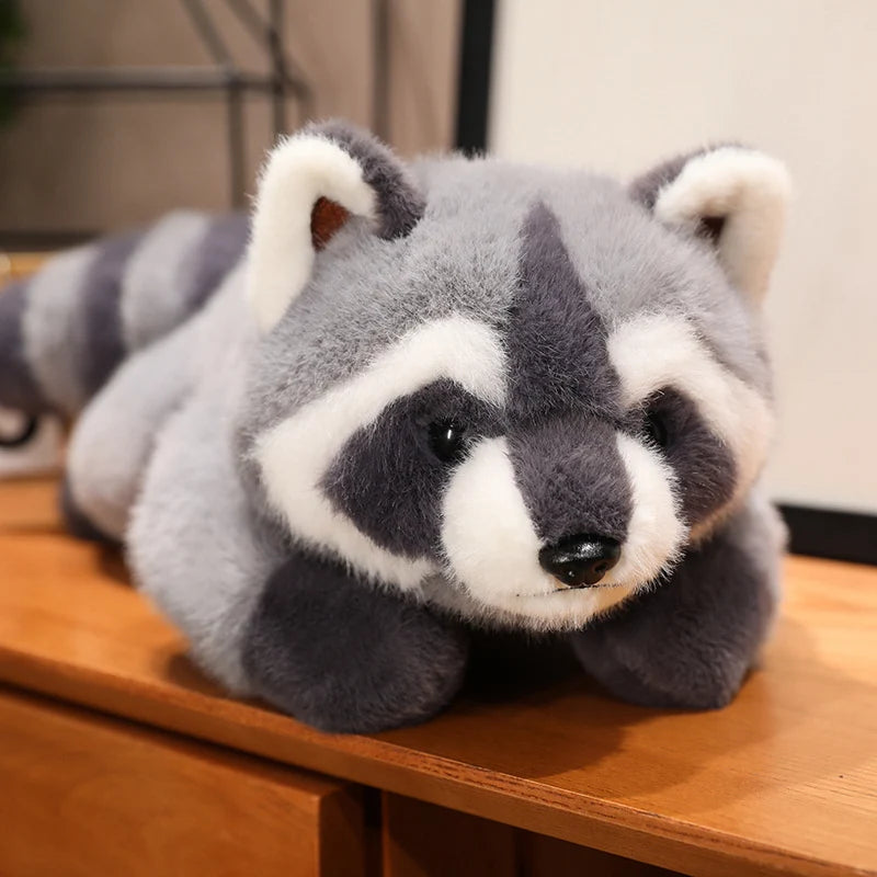A gray and white raccoon plush toy lying on a wooden surface.