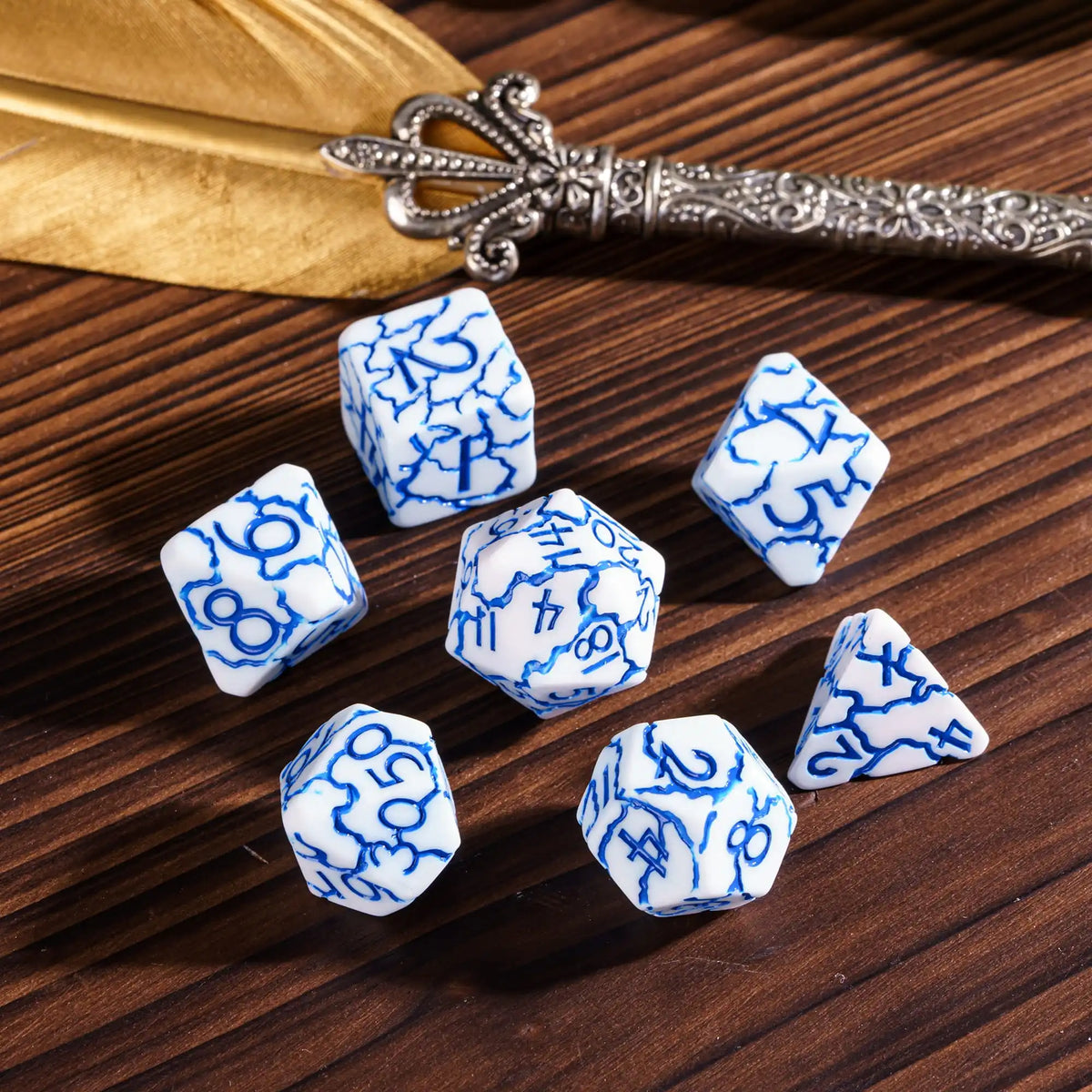 A set of seven frosted blue and white polyhedral dice resting on a dark wooden surface next to an ornate silver dagger.