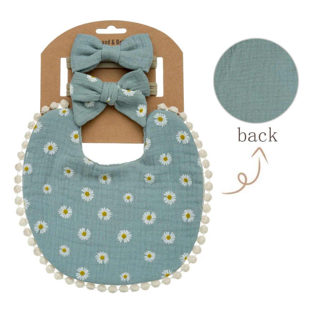 A light blue floral fabric bib and matching bow headband set displayed on a cardboard backing.