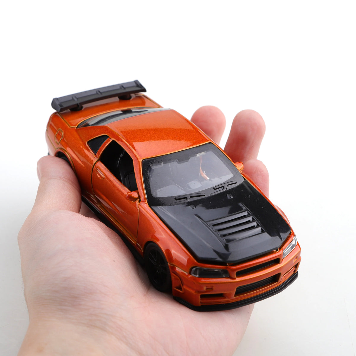 An orange 1/36 scale die-cast sports car with pull-back action is held in a person's hand.