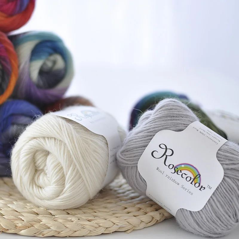 A ball of light gray wool yarn labeled Rosecolor from the Wool Rainbow Series resting on a woven mat.
