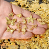 A hand holds various gold-colored mixed metal charms including a butterfly, star, and cross for DIY jewelry making.