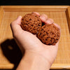A hand holds a brown, textured walnut ball on a wooden tray.