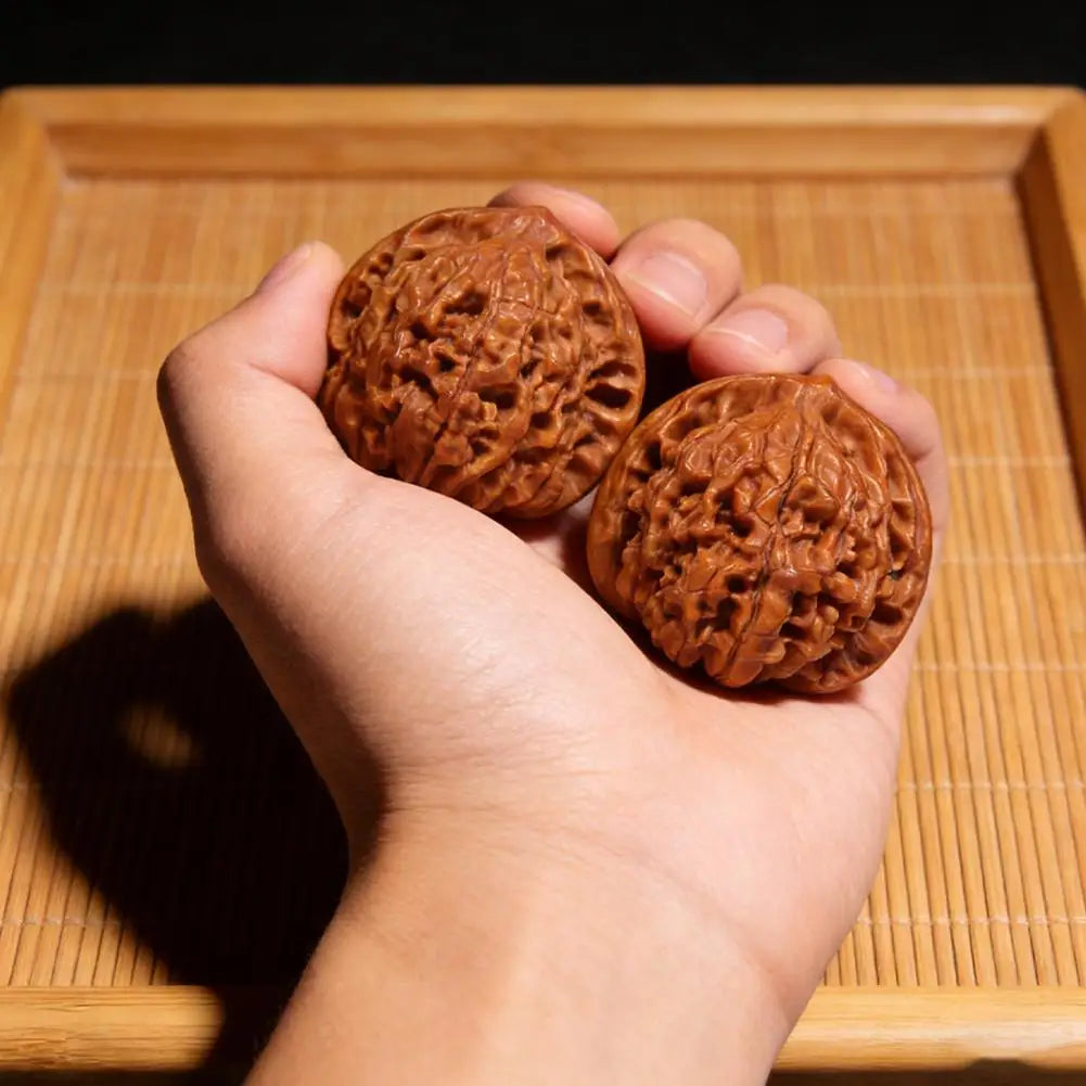 A hand holds a brown, textured walnut ball on a wooden tray.