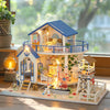 A detailed miniature dollhouse kit of a seaside beach house with blue accents and LED lights on a wooden base.