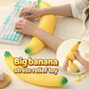 Hands are squeezing a large yellow banana stress relief toy on a white surface.