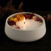 A white silicone mold filled with dried flowers and a lit candle on a dark wooden surface.
