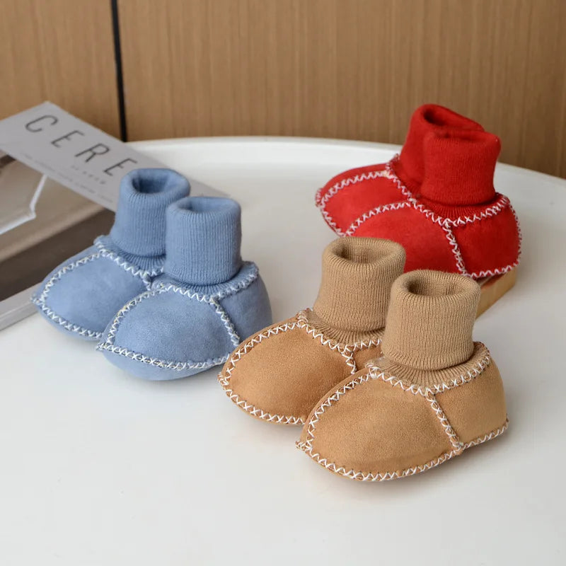 A set of cozy suede baby booties in blue and tan with plush fur lining displayed on a white surface.