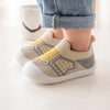 A pair of beige and yellow breathable anti-slip baby first walker shoes worn by a child.