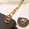 Close-up of a gold-tone metal D-ring buckle clip attached to a black leather bag strap.