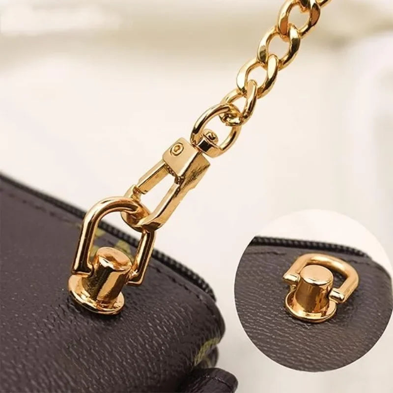 Close-up of a gold-tone metal D-ring buckle clip attached to a black leather bag strap.